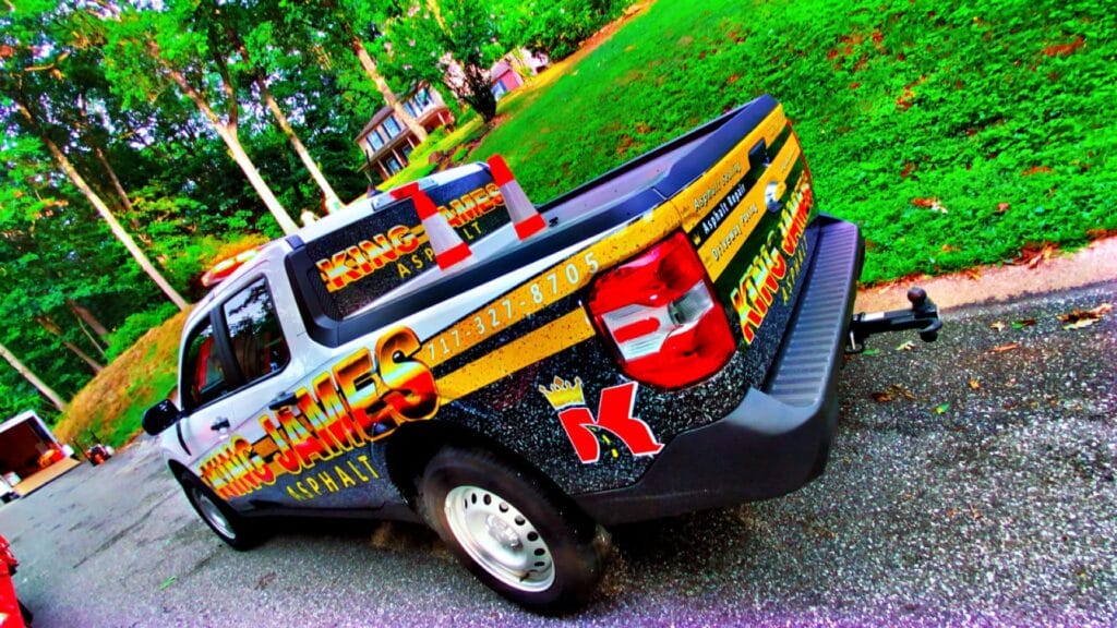 A pickup truck with "King James Asphalt" branding and contact information is parked on a residential street next to a grassy yard.