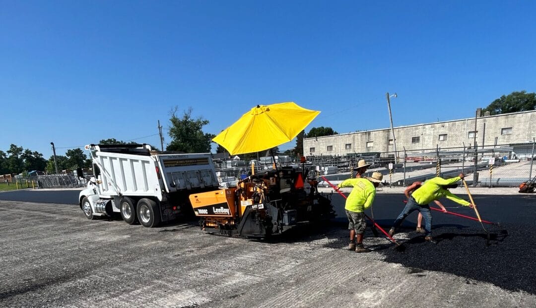 Workers paving asphalt under yellow umbrella